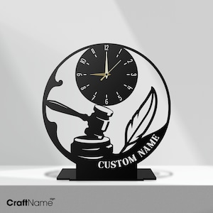 May include: Black metal clock featuring a gavel, a feather, and the text "CUSTOM NAME".