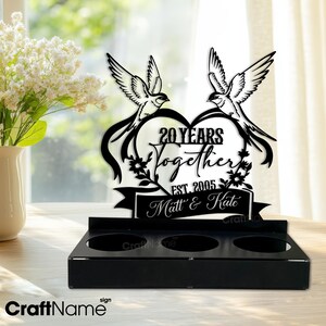 Puede incluir: Letrero de aniversario de metal negro con dos p&aacute;jaros, un coraz&oacute;n y las palabras "20 Years Together" y "Matt & Kate". El letrero tiene una base con tres aberturas circulares. El texto "CraftName" est&aacute; en la parte inferior.