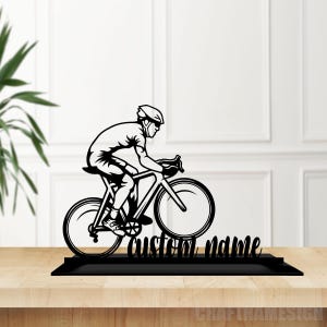 May include: Black silhouette of a cyclist riding a bicycle with the text "custom name" below. The silhouette is on a black base.
