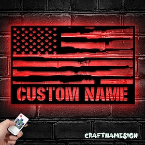 May include: A rectangular black metal wall sign featuring a cutout design of the American flag with rifle silhouettes forming the stripes and stars in the canton. The sign is backlit with a vibrant red LED glow and displays the text CUSTOM NAME.