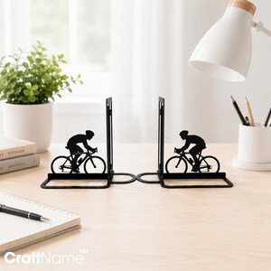 May include: A pair of black metal bookends featuring a silhouette of a cyclist riding a road bike. Each bookend has a flat base and an upright panel displaying the rider in a forward-leaning position, designed to support books on a flat surface.