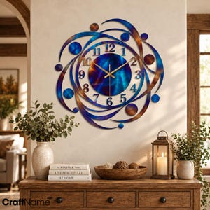 May include: A circular wall clock featuring a metallic blue and copper finish with swirling abstract metal accents. The clock face displays black Arabic numerals from 1 to 12 and thin gold-toned hands. The center of the clock has a deep blue hue.