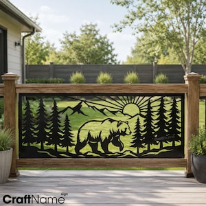 May include: A black metal decorative railing panel featuring a laser-cut design of a walking bear in the foreground, surrounded by pine trees, mountains, and a sunburst pattern in the background. The panel is mounted within a wooden deck railing.