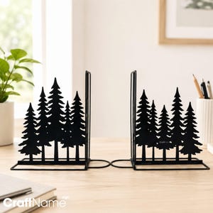 May include: A pair of black metal bookends featuring a silhouette design of a dense pine forest. Each bookend has a flat base and a vertical support panel cut into the shape of multiple evergreen trees of varying heights and sizes.