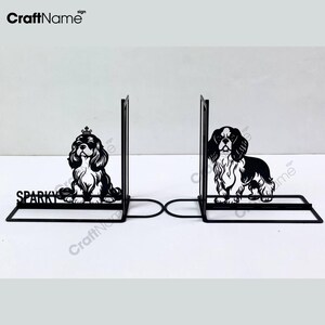 Könnte beinhalten: Schwarze Metall-Buchstützen mit einer Silhouette eines Cavalier King Charles Spaniel Hundes auf jeder Seite. Die linke Buchstütze hat das Wort "Sparky" auf der Basis.