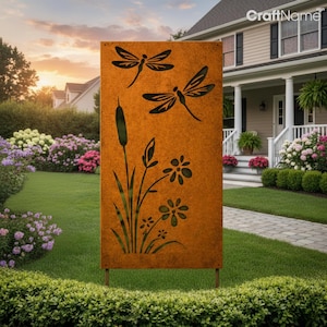 May include: A rectangular, rust-colored metal garden art piece featuring cut-out designs of dragonflies, cattails, and flowers. The artwork is mounted on two metal stakes and is displayed outdoors in front of a house with a well-manicured lawn and garden.