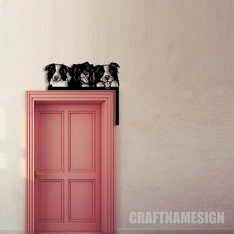 K&ouml;nnte beinhalten: Drei schwarze und wei&szlig;e Border-Collie-Hundek&ouml;pfe, die &uuml;ber einer rosafarbenen T&uuml;r mit einem goldenen T&uuml;rgriff gucken. Die Metall-Hunde-K&ouml;pfe sind ein an der Wand montiertes T&uuml;rschild mit dem Text "CRAFTNAMESIGN" unter der T&uuml;r.