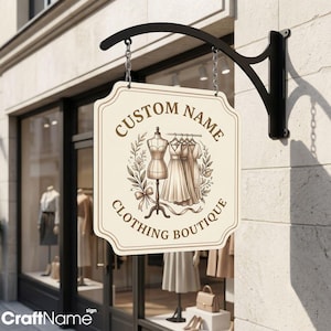Könnte beinhalten: Ein cremefarbenes, rechteckiges Hängeschild mit dekorativen Kanten, das an Ketten an einer schwarzen Metallhalterung befestigt ist. Das Schild zeigt den braunen Schriftzug CUSTOM NAME CLOTHING BOUTIQUE, zentriert um eine Abbildung von Schneiderpuppe und Kleidern.