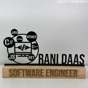 May include: A black metal desk sign featuring a computer monitor icon surrounded by programming language logos including Java, HTML5, Python, C#, C++, and JS. The name RANI DAAS is cut out in black metal, mounted on a light wood base labeled SOFTWARE ENGINEER.
