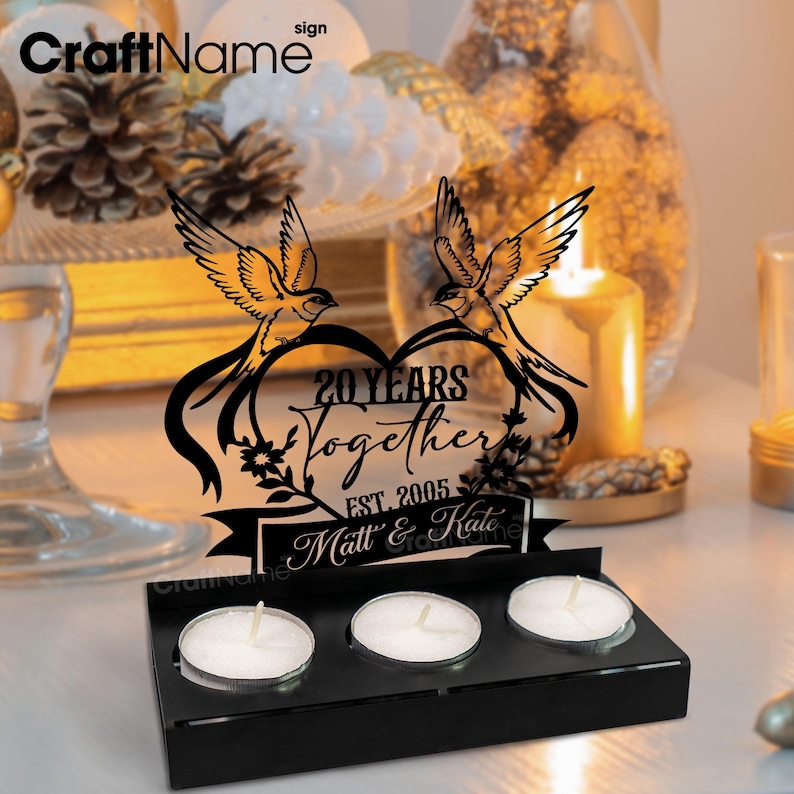 Puede incluir: Portavelas de aniversario negro cortado con l&aacute;ser con el texto "20 Years Together" y los nombres "Matt & Kate". El dise&ntilde;o presenta dos p&aacute;jaros sobre un coraz&oacute;n. Incluye tres velas de t&eacute;.