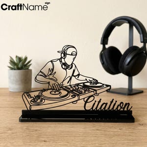 May include: A black, laser-cut acrylic sign featuring a continuous line art illustration of a DJ wearing a cap and headphones while operating a turntable console. The word Citation is written in script font on the base of the display stand.