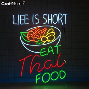May include: Neon sign with the text "Life is short, eat Thai food". The sign features a bowl of noodles with shrimp and vegetables in a white outline. The text is in various colors, including white, green, red, and yellow.