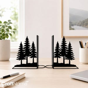 May include: A pair of black metal bookends featuring a silhouette design of three pine trees on a base. The metal cutouts depict a forest scene with varying tree heights, providing a sturdy support for books with a clean, flat-edged vertical spine.