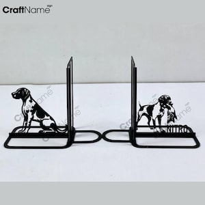 Op de afbeelding: Zwarte metalen boekenleggers met een silhouet van een hond aan elke kant. De boekenlegger aan de linkerkant heeft een hond die zit, terwijl de boekenlegger aan de rechterkant een hond heeft die staat met een vogel in zijn bek. De tekst "NITRO" staat gedrukt op de rechter boekenlegger.