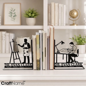 May include: A pair of black metal bookends featuring silhouettes of a person painting at an easel and a person working at a desk with a lamp. Both bookends include the text DR. EVAN CLARK in a bold, sans-serif font at the base of the design.