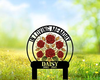 May include: A black circular memorial garden stake featuring a bouquet of red roses with gold leaves in the center. The text "IN LOVING MEMORY" is arched along the top, while the name "DAISY" and the dates "2005 - 2025" are printed below.