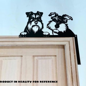 K&ouml;nnte beinhalten: Schwarze Metallsilhouette von zwei Zwergschnauzern, die &uuml;ber eine Holzt&uuml;r schauen. Die Silhouette ist mit einer Metallhalterung am T&uuml;rrahmen befestigt.