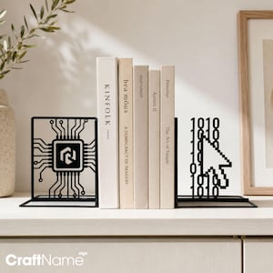 May include: A pair of black metal bookends featuring a computer chip design on the left and a pixelated cursor with binary code on the right, supporting a row of five neutral-colored books standing upright on a flat surface.
