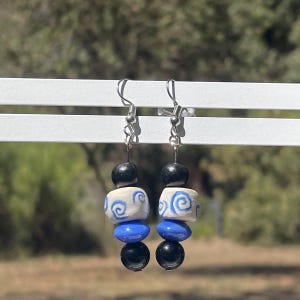 May include: A pair of dangle earrings featuring blue and white ceramic beads and black beads. The earrings have silver hooks.