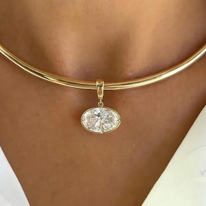 May include: A gold-colored necklace with a pendant featuring an oval-cut diamond. The necklace is a simple, elegant design, perfect for everyday wear. The pendant is suspended from a delicate chain.