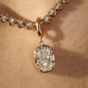May include: A gold necklace with a diamond pendant. The necklace has small, round diamonds set in a gold chain. The pendant is an oval-shaped diamond, set in gold.