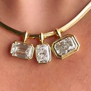 Könnte beinhalten: Eine goldene Halskette mit drei Diamantanhängern in verschiedenen rechteckigen Formen. Die Diamanten sind in goldenen Fassungen gefasst und hängen an einer goldenen Kette. Die Halskette wird um den Hals getragen.
