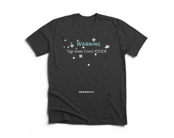 May include: A charcoal grey short-sleeve t-shirt featuring white star graphics and the text "WARNING This Shirt Costs 1000$" in white and light blue. Below the stars, the text "I'M WORTH IT" is printed in small white capital letters.