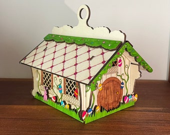 May include: A wooden Easter house ornament with a white and pink roof, green vines, and a brown door. The house is decorated with colorful Easter eggs.