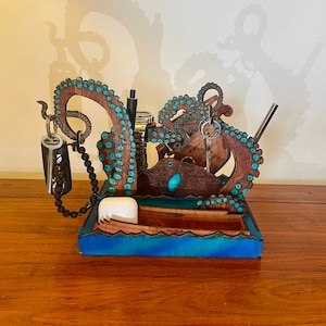 Könnte beinhalten: Ein hölzerner Oktopus-förmiger Schreibtisch-Organizer mit blauen und braunen Akzenten. Er verfügt über ein kleines, bootförmiges Fach, einen Schlüsselhalter und einen Platz für ein Telefon oder andere kleine Gegenstände.