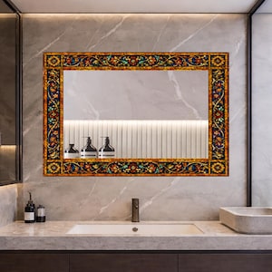 May include: A rectangular mirror with a decorative frame featuring a floral design in shades of red, blue, yellow, and green. The mirror is mounted above a bathroom sink with a marble countertop and a gray wall.