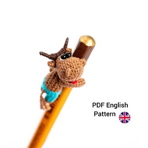 Op de afbeelding: Haak amigurumi patroon voor een bruine stier met een blauwe broek, die een potlood vasthoudt. PDF-patroon in het Engels.