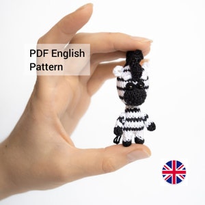 May include: A crocheted zebra toy with black and white stripes. The zebra is small and is being held in a person's hand. The toy has black eyes and a black nose. The image includes the text "PDF English Pattern".