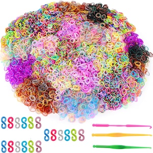 Könnte beinhalten: Ein großer Haufen bunter Gummibänder in verschiedenen Schattierungen von Rosa, Blau, Grün, Gelb, Orange und Braun. Es gibt drei Plastik-Häkelnadeln in Rosa, Orange und Grün.