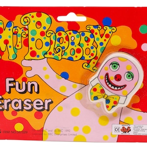 Könnte beinhalten: Ein rosa Mr. Blobby Radiergummi mit gelben Punkten und einer gelben Schleife. Der Radiergummi befindet sich auf einem roten, gelben und grünen Hintergrund mit dem aufgedruckten Text "Mr. Blobby Fun Eraser". Die Verpackung enthält auch den Text "Mr. Blobby and BBC 1992. Licensed by BBC Enterprises Limited. Item No. 39/029."