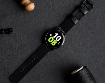 Peut inclure: Un bracelet de montre en cuir noir avec un cadran de montre intelligente noir affichant l'heure 10:08. Le bracelet de montre présente des détails de couture et une fermeture à boucle.