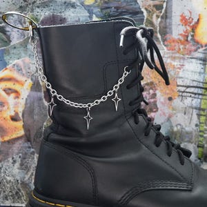 Puede incluir: Botas de cuero negro con una cadena plateada y abalorios de estrellas unidos a la parte superior de la bota.