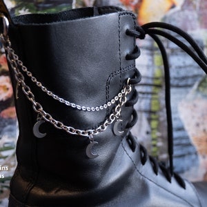 Puede incluir: Bota de cuero negro con cadenas plateadas y colgantes de luna. Las cadenas est&aacute;n unidas a los ojales de la bota. El texto de la imagen dice "2 tipos de cadenas, 4 colgantes de luna."