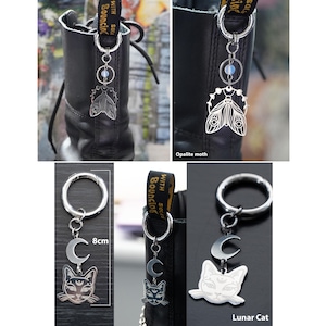 K&ouml;nnte beinhalten: Silberfarbene Stiefelanh&auml;nger mit einem Opalit-Motten- und Mondkatzen-Design. Der Katzenanh&auml;nger ist 8 cm lang. Die Anh&auml;nger sind an einem silbernen Ring befestigt, der an Stiefeln befestigt werden kann.