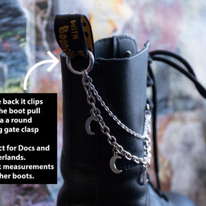 Puede incluir: Bota de cuero negro con cadena plateada y colgantes de luna. La cadena se sujeta a la leng&uuml;eta de la bota con un mosquet&oacute;n redondo. La bota tiene las palabras "WITH BOUNCING SOLES" impresas en la leng&uuml;eta.