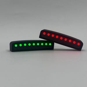May include: Two black, rectangular LED light bars. One bar displays green lights, the other red. The lights are evenly spaced and appear to be embedded in the black casing. The bars are slightly curved and have a modern design.