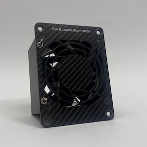 May include: A black and gray fan with a carbon fiber weave pattern. The fan has a square frame with the text "SIMRACINGCRAFTSMEN" printed on it. The fan blades are visible behind the frame.