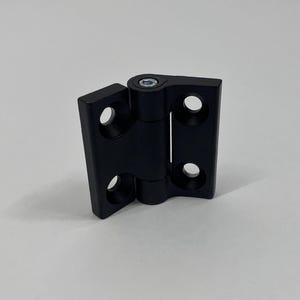 Puede incluir: Una bisagra negra con un pivote central y múltiples orificios para tornillos. La bisagra está hecha de un material sólido y está diseñada para diversas aplicaciones. La bisagra se muestra sobre un fondo blanco.