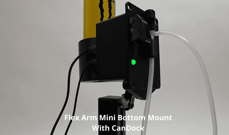 May include: A black Flex Arm Mini Bottom Mount with CanDock featuring a carbon fiber textured plate, a bright green LED indicator light, two black electrical cables, and a clear plastic tube connected to a black nozzle on a vertical support.