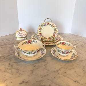 Könnte beinhalten: Ein Vintage-Teeservice von Royal Crown Derby mit floralen Mustern. Das Set umfasst zwei Tassen mit Untertassen, eine Suppenschüssel mit Untertasse und mehrere Teller. Die Teile sind weiß mit bunten Blumenmustern und goldenen Verzierungen.