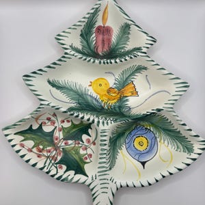 Può includere: Un vassoio da portata in ceramica a forma di albero di Natale con tre sezioni. Le sezioni sono decorate con una candela, un uccello giallo, agrifoglio e un ornamento blu. L'albero è bianco con accenti verdi e rossi.