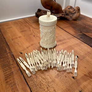 May include: A set of 24 white plastic forks with ornate designs, stored in a white plastic container with a floral design. The container has a lid with a small flower on top.