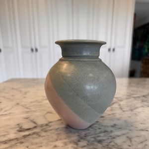 May include: A grey and pink ceramic vase with a speckled glaze. The vase has a rounded body and a flared rim.