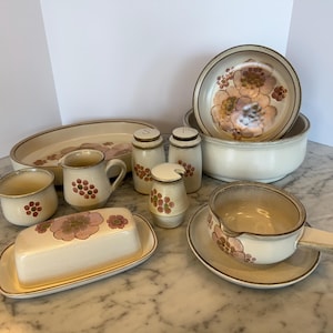 Puede incluir: Un juego de vajilla de cocina de gres vintage con un patrón floral. El juego incluye una mantequillera, una jarra de crema, un azucarero, dos saleros y pimenteros, una salsera con un platillo y una fuente ovalada grande.