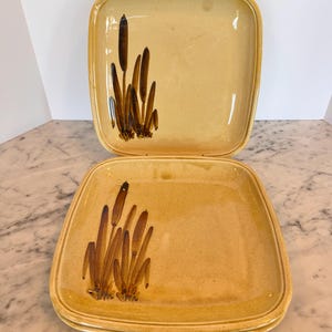 May include: Set of three square ceramic plates with a brown and yellow glaze. The plates feature a brown stylized design of reeds or cattails.
