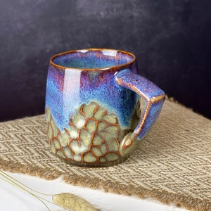 The photo shows a handmade cup with a square handle with a volume of 350 ml. It is textured and brown on the bottom, smooth and iridescent on top. This is our bestseller.